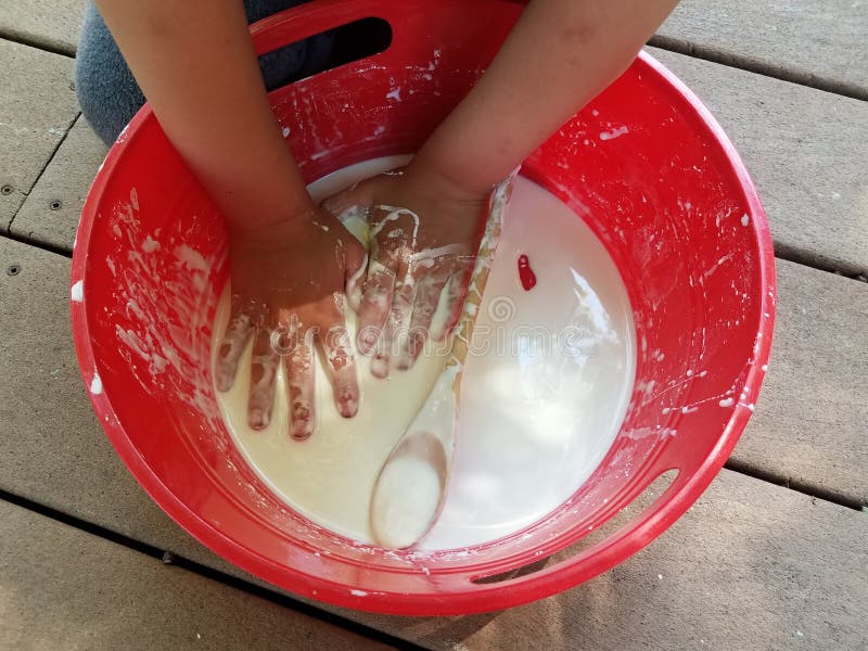 Kid with hands playing in red bucket with white slime on deck