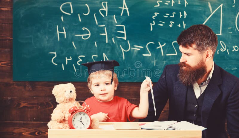 Kid happy studies individually with father, at home. Individual schooling concept. Teacher and pupil in mortarboard stock photography Kid happy studies individually with father, at home. Individual schooling concept. Teacher and pupil in mortarboard stock photography