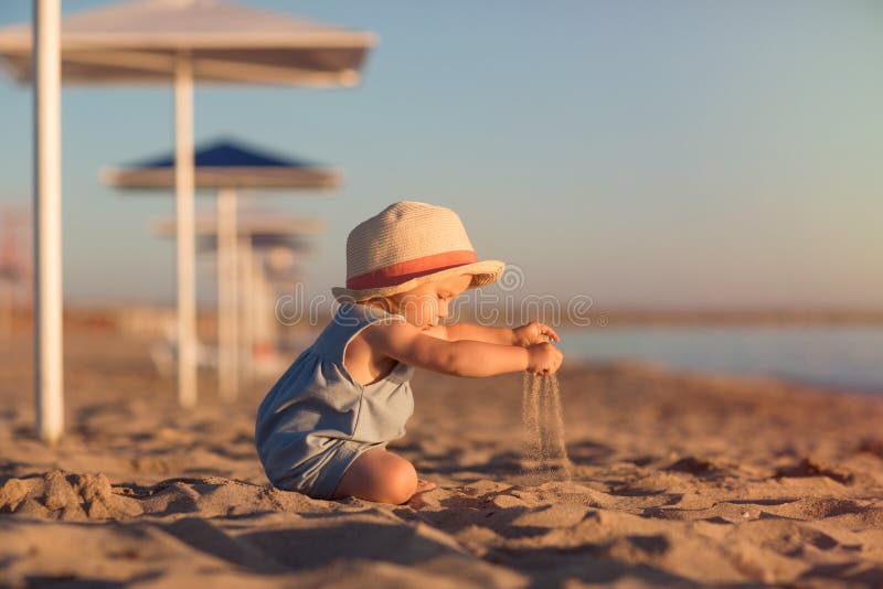 Kid in a hat playing with sand on the beach by the sea. holidays with children near the ocean