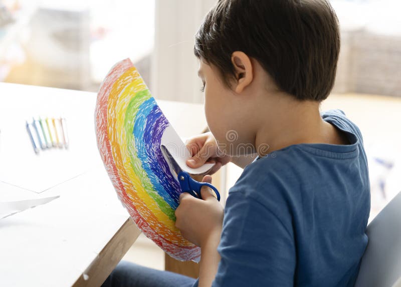 Kid is isolation using scissors cutting paper in rainbow shape on white background, Children activities at home while school off. royalty free stock images