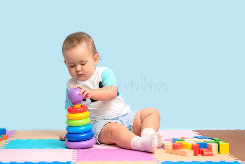 A kid of 15-23 months is sitting and assembling a pyramid toy, putting colorful rings on the plastic base of the tower royalty free stock photos