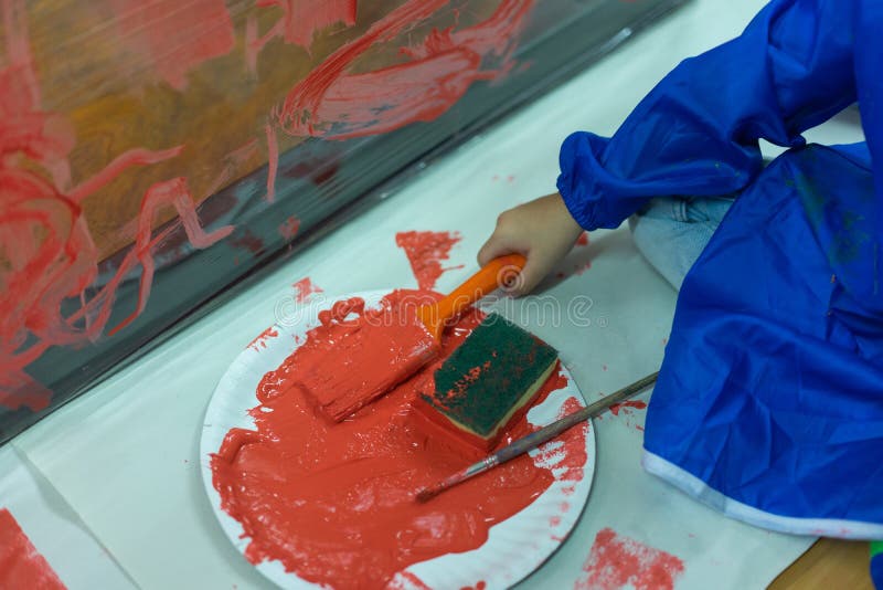 Kid is Painting the Plastic Wall with Red Color. Stock Photo Image of