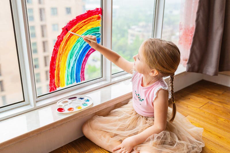 Kid painting rainbow during Covid-19 quarantine at home. Girl near window. Stay at home Social media campaign for coronavirus stock images Kid painting rainbow during Covid-19 quarantine at home. Girl near window. Stay at home Social media campaign for coronavirus stock images