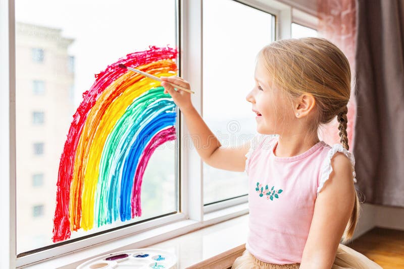 Kid painting rainbow during Covid-19 quarantine at home. Girl near window. Stay at home Social media campaign for coronavirus stock photo Kid painting rainbow during Covid-19 quarantine at home. Girl near window. Stay at home Social media campaign for coronavirus stock photo