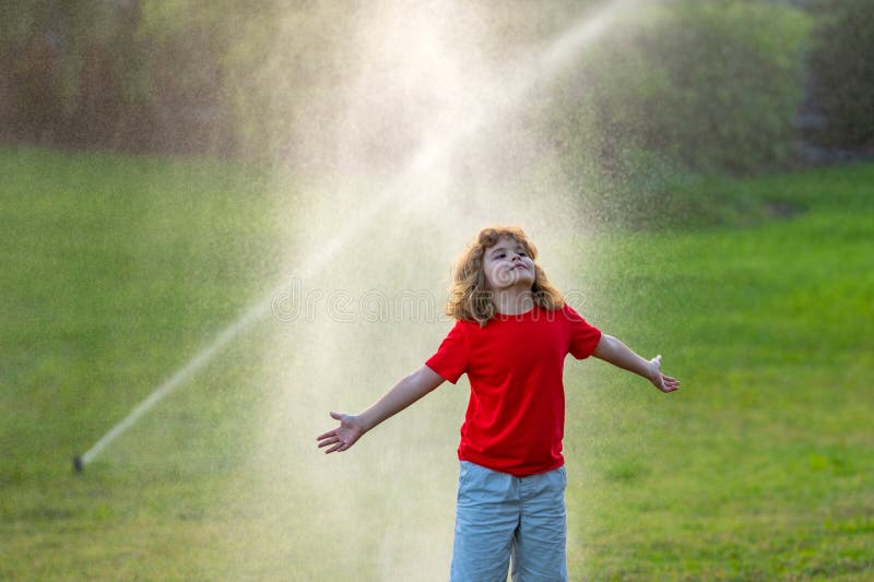 Kid play in garden near irrigation watering sprinkler system. Watering grass with automatic sprinkler. Lawn and royalty free stock photo