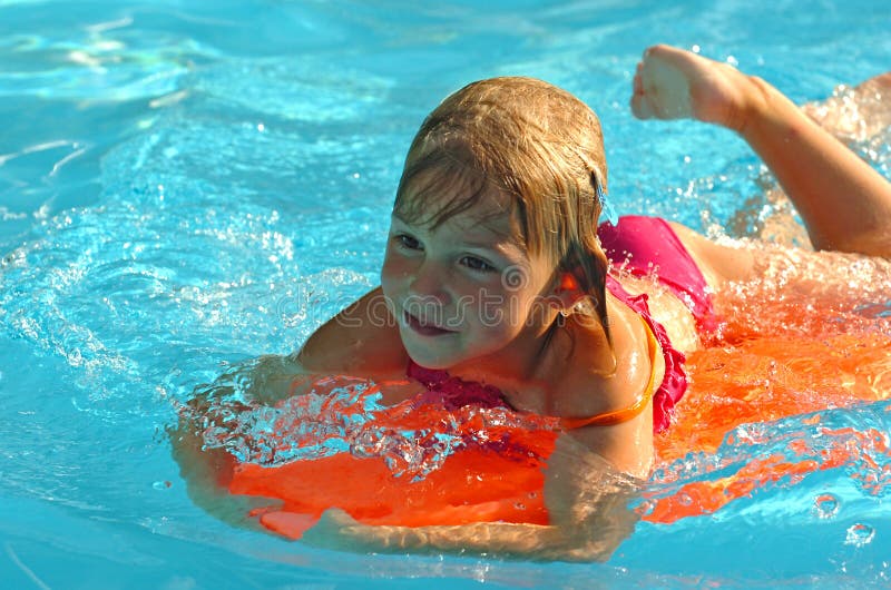 Bambina che gioca su un arancio consiglio di divertimento in piscina blu acqua con una faccia buffa espressione in viso.