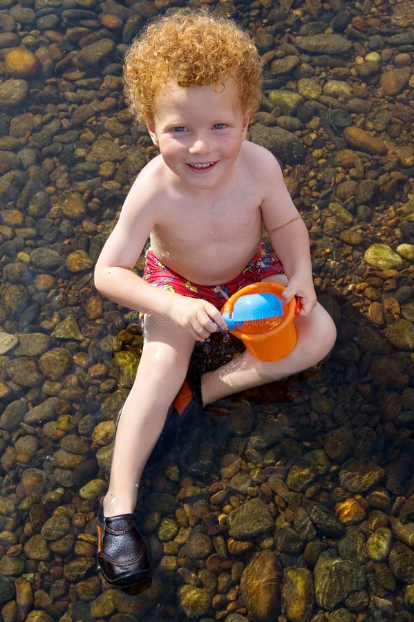 Joven chico (3) en Agua, feliz buscando arriba, juguete cucharón a balde.