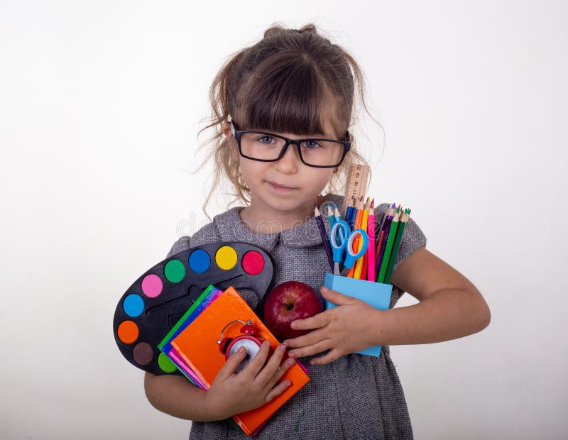 Kid ready for school. Cute clever child in eyeglasses holding school supplies: pens, notebooks, scissors and apple.