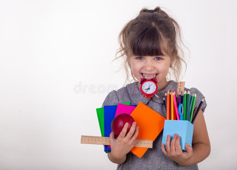 Kid ready for school. Cute clever child in eyeglasses holding school supplies: pens, notebooks, scissors, alarm clock and apple.