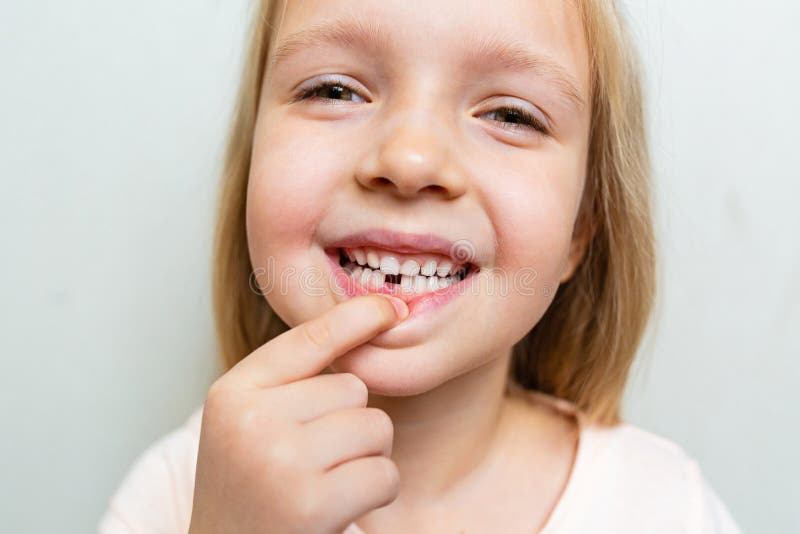 Kid showing the first milk tooth. Change teeth concept. Cute little girl with blonde hair on gray background with copy space stock images Kid showing the first milk tooth. Change teeth concept. Cute little girl with blonde hair on gray background with copy space stock images