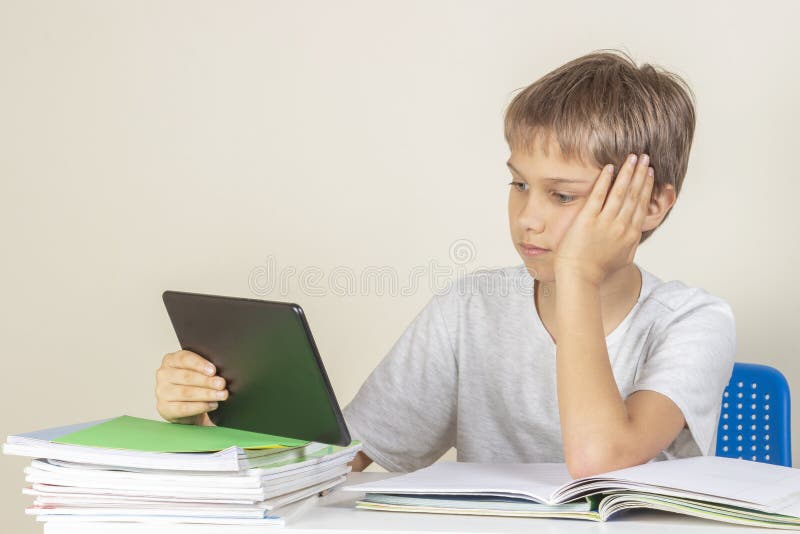Kid sitting at table with books notebooks and using tablet computer stock image Kid sitting at table with books notebooks and using tablet computer stock image