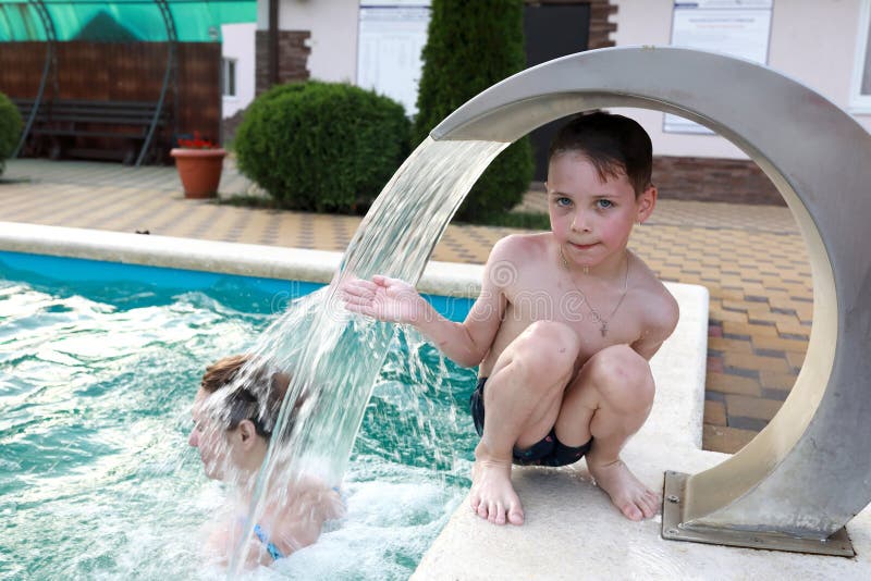 Kid sitting under stream of water in pool