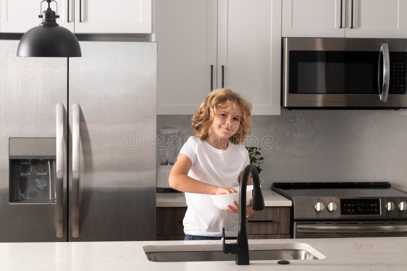 Kid washing dishes in the kitchen interior. Child helping his parents with housework. Child boy washing dishes in the stock photo