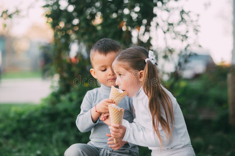 Kids Boy and girl eating ice cream outdoors on grass and trees background