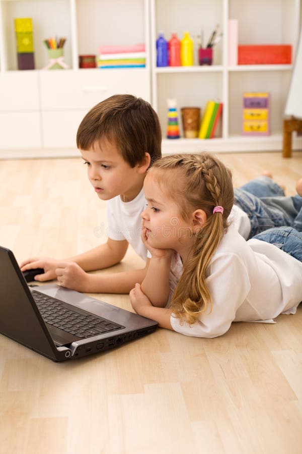 Kids busy and concentrated working on a laptop laying on the floor in their room