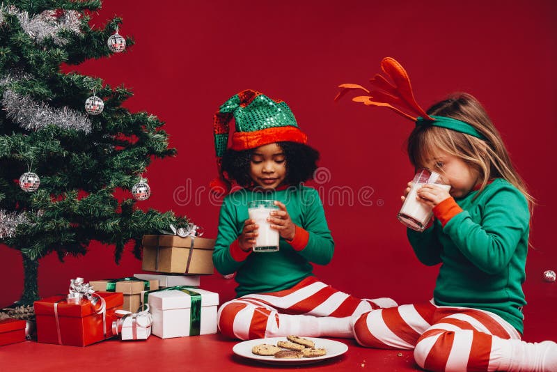 Kids drinking milk sitting beside a christmas tree royalty free stock photography Kids drinking milk sitting beside a christmas tree royalty free stock photography