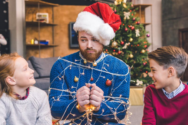 Adorable little kids and father tied up with christmas garland.