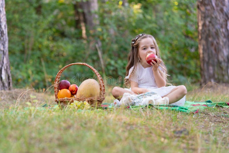 Kids forest picnic. Child with basket of autumn fruits eating apple. Toddler kid in sunny park. Little girl enjoying