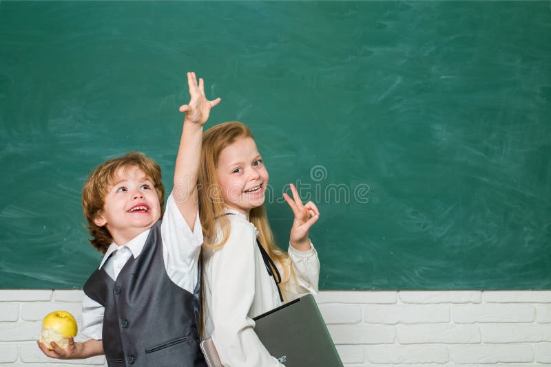 Kids gets ready for school. Couple of little girl and boy in classroom. Schoolgirl helping pupils studying at desks in classroom. Happy school kids. Apple and books - school concept