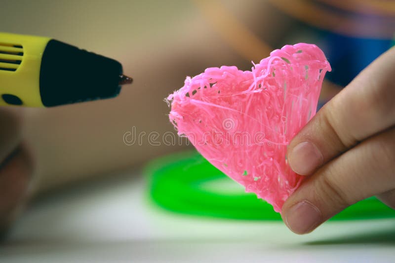 Kids hand holding yellow 3D printing pen with filaments and makes heart on white background. Top view. Copy space for