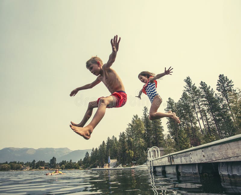 Kids jumping off the dock into a beautiful mountain lake royalty free stock image
