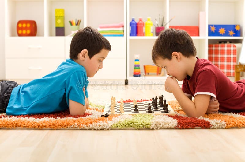 Serious kids playing chess laying on the floor in their room