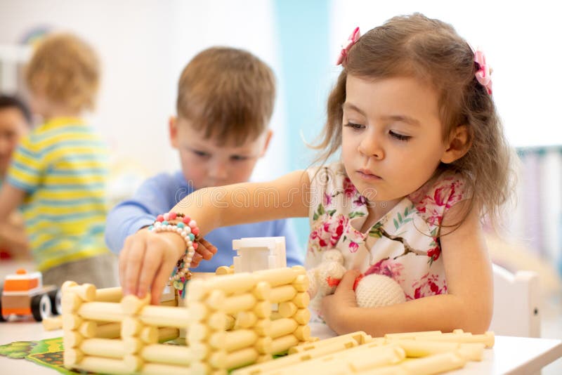 Kids playing in kindergarten. Children building toy house with plastic blocks sitting together by the table