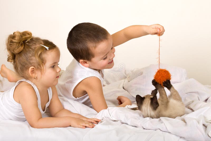 I bambini a giocare con un gattino e un filo di palla di posa sul letto.