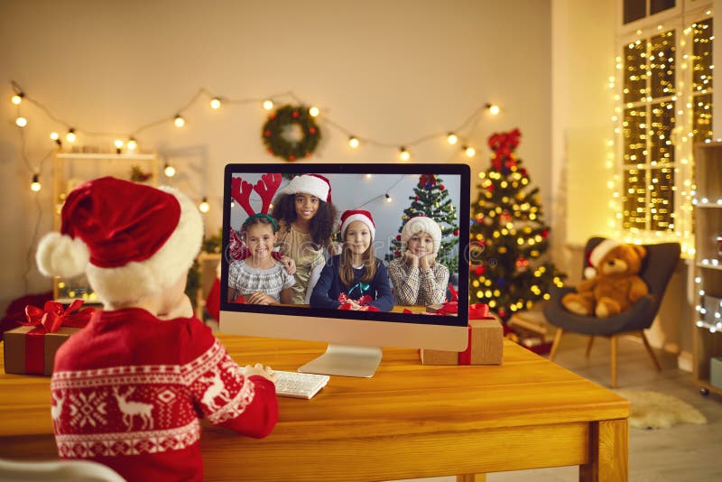 Little boy sitting at computer and video calling his friends to stay in touch during winter break