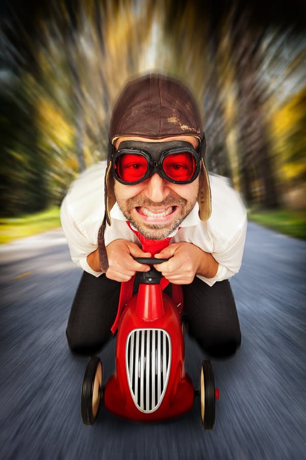 Man in retro racing hat and goggles driving on toy car at speed with blurred background. Man in retro racing hat and goggles driving on toy car at speed with blurred background.