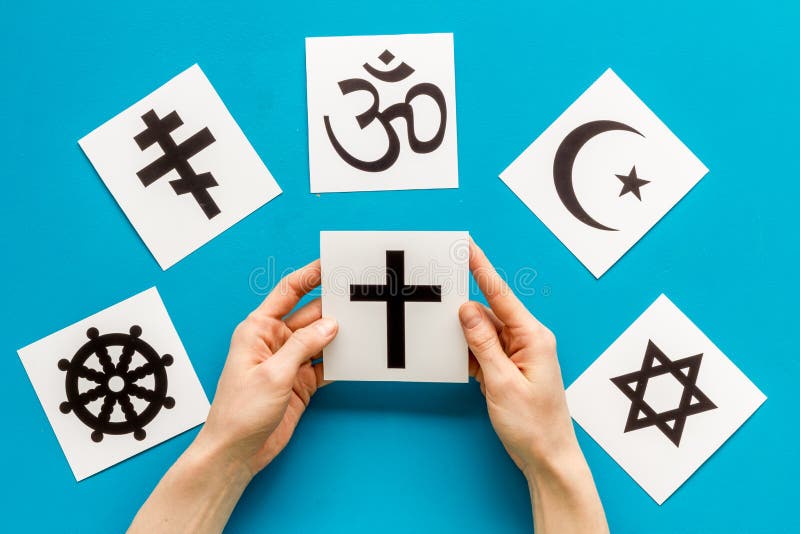Kies het religie concept. hand met katholieke kruising bij wereldreligies symbolen op blauwe achtergrond bovenaanzicht