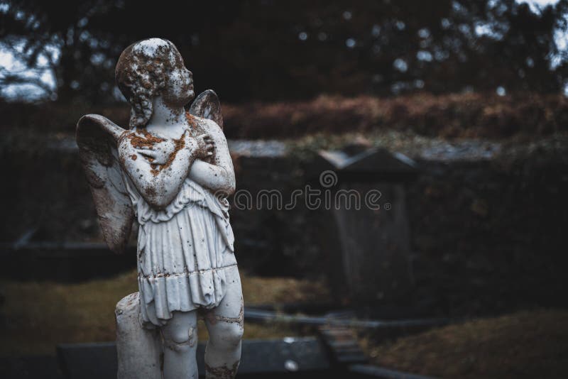 KILKENNY, IRLAND, DECEMBER 23, 2018: Skulptur av en gammal krämig körsbärsängel mitt i en kyrkogård full av lichen och