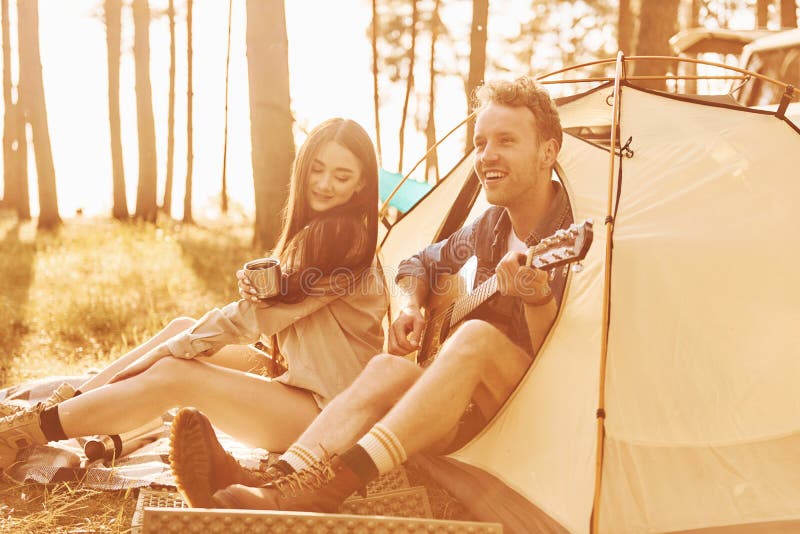 Kille som spelar gitarr. Unga par reser i skogen på dagtid tillsammans fotografering för bildbyråer