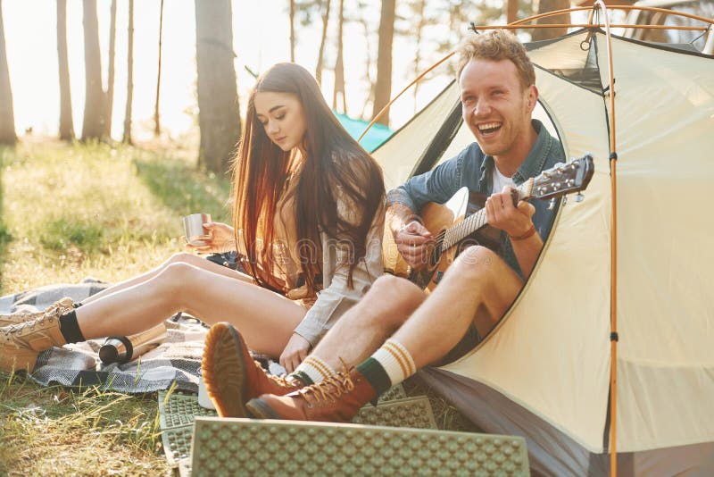 Kille som spelar gitarr. Unga par reser i skogen på dagtid tillsammans arkivbild