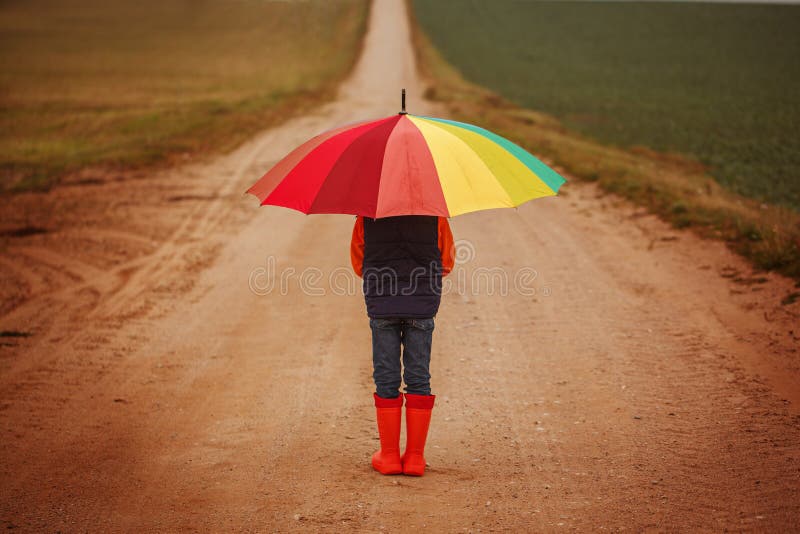 Kind die in oranje rubberlaarzen kleurrijke paraplu houden onder regen in de herfst Achter mening stock afbeeldingen Kind die in oranje rubberlaarzen kleurrijke paraplu houden onder regen in de herfst Achter mening stock afbeeldingen