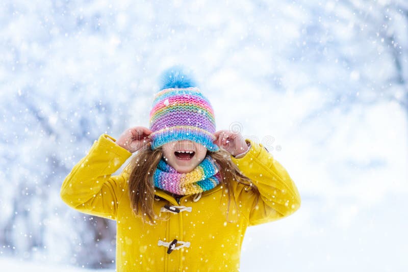 Child in knitted hat playing in snow on Christmas vacation. Winter outdoor fun. Knitting and outerwear for family. Kids play in snowy park. Little girl in knit scarf and mittens catching snowflakes. Child in knitted hat playing in snow on Christmas vacation. Winter outdoor fun. Knitting and outerwear for family. Kids play in snowy park. Little girl in knit scarf and mittens catching snowflakes