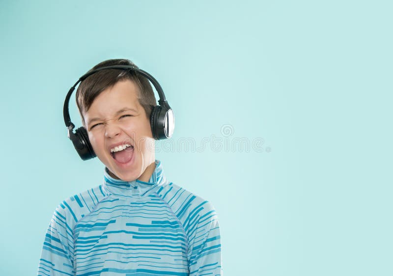 Kid enjoying music on his headphones, listening to music. Handsome young stylish kid in headphones standing against blue background and smiling. Kid enjoying music on his headphones, listening to music. Handsome young stylish kid in headphones standing against blue background and smiling.