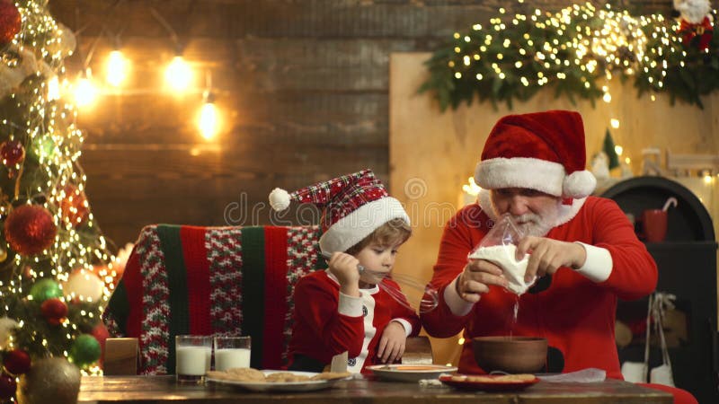 Kind und Santa Claus, die in gedientem Lebkuchenkuchen genießen Santa Grandfather und Enkel, die Spaß Nähe Weihnachtsbaum haben