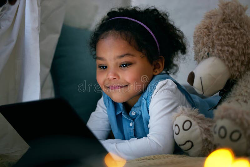 Kind und Tablett zum Nachts Filmschauen in Festzelt und Teddybär für Freundschaft. Kind von weiblichen Personen und Online-Abonnement für Streaming-Cartoserie Internet-Video-und entspannen.