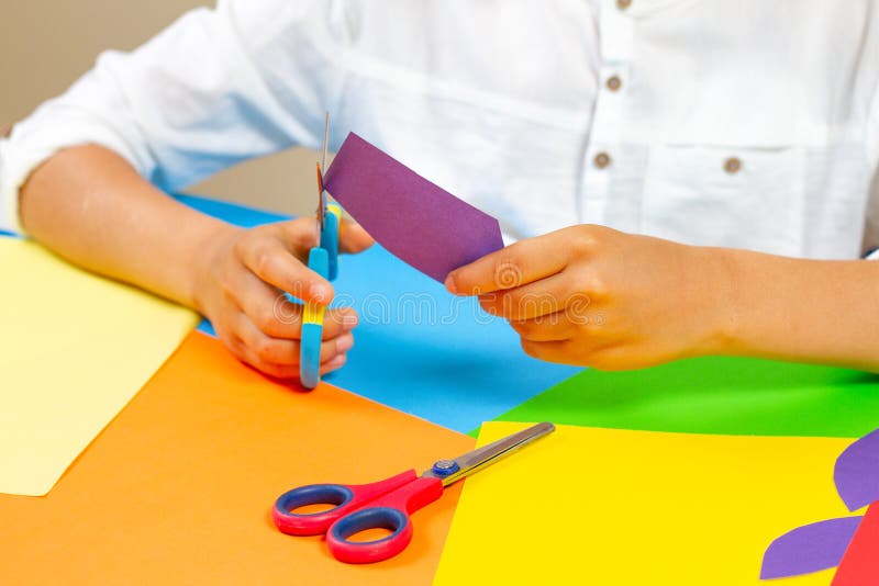 Kind übergibt farbiges Papier des Ausschnitts mit Scheren am Tisch lizenzfreie stockfotos Kind übergibt farbiges Papier des Ausschnitts mit Scheren am Tisch lizenzfreie stockfotos