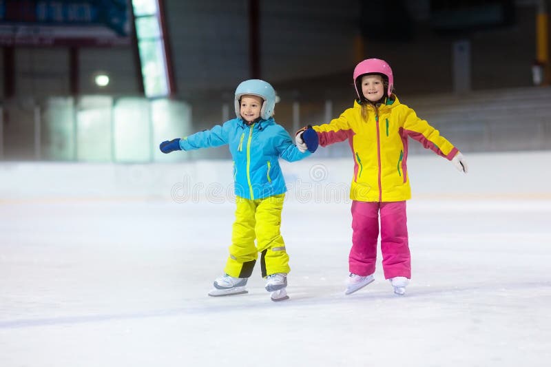 Children skating on indoor ice rink. Kids and family healthy winter sport. Boy and girl with ice skates. Active after school sports training for young child. Snow fun activity by cold weather. Children skating on indoor ice rink. Kids and family healthy winter sport. Boy and girl with ice skates. Active after school sports training for young child. Snow fun activity by cold weather.