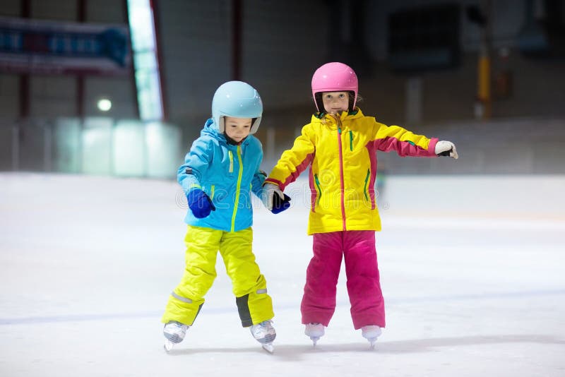 Children skating on indoor ice rink. Kids and family healthy winter sport. Boy and girl with ice skates. Active after school sports training for young child. Snow fun activity by cold weather. Children skating on indoor ice rink. Kids and family healthy winter sport. Boy and girl with ice skates. Active after school sports training for young child. Snow fun activity by cold weather