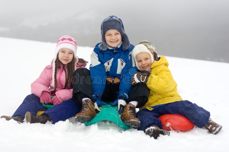 Three children stop their downhill sliding fun long enough to pose for this picture in the snow on a wintry day. Three children stop their downhill sliding fun long enough to pose for this picture in the snow on a wintry day.