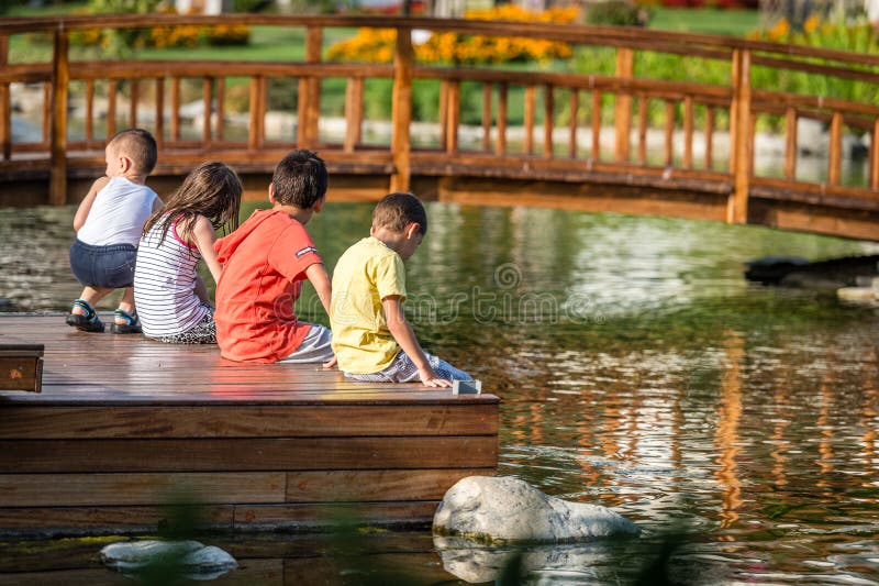 Kinder, Die Im Park Nahe Bei Dem Teich Sitzen Redaktionelles Bild