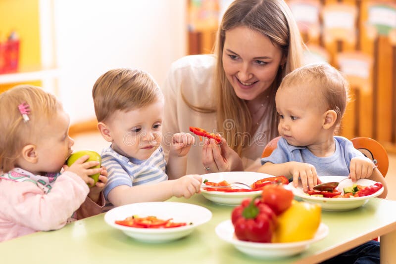 Kinder essen in der Kindertagesst?ttenmitte zu Mittag Kinder, die gesunde Nahrung im Kindergarten essen Kindergärtnerin mit Babys