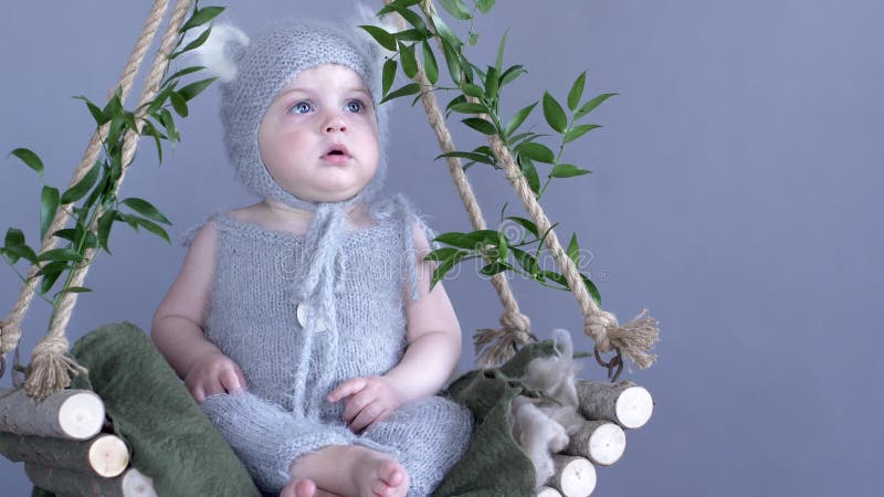 Kinder setzen, Baby mit großen Augen in der Miezekatze Zeit fest, die Kostüm auf dem hölzernen Schwingen sitzt, das mit grünen Ni