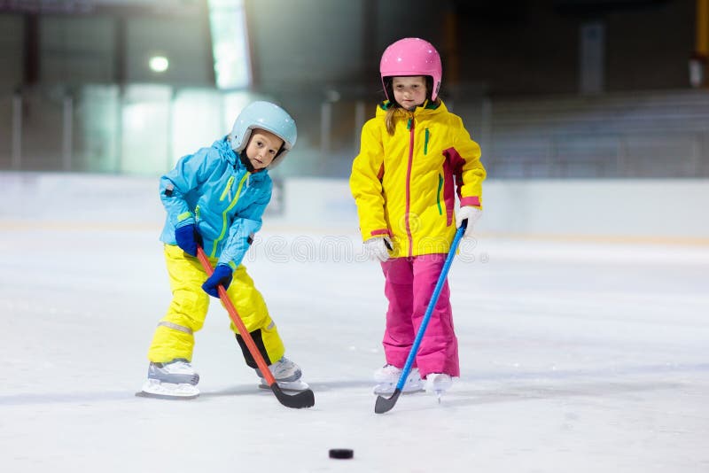 Children play ice hockey on indoor rink. Healthy winter sport for kids. Boy and girl with hockey sticks hitting puck. Child skating. Little kid on sports training after school. Snow and ice fun. Children play ice hockey on indoor rink. Healthy winter sport for kids. Boy and girl with hockey sticks hitting puck. Child skating. Little kid on sports training after school. Snow and ice fun