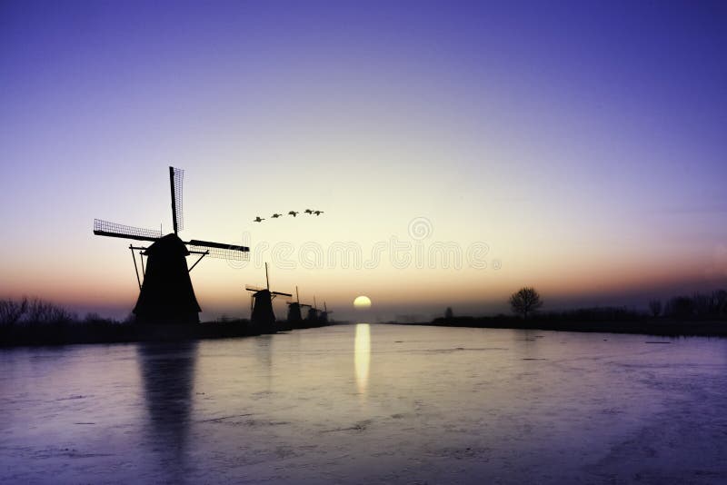 Kinderdijk - χήνες που πετούν πέρα από την ανατολή στην παγωμένη ευθυγράμμιση ανεμόμυλων στοκ φωτογραφία με δικαίωμα ελεύθερης χρήσης Kinderdijk - χήνες που πετούν πέρα από την ανατολή στην παγωμένη ευθυγράμμιση ανεμόμυλων στοκ φωτογραφία με δικαίωμα ελεύθερης χρήσης
