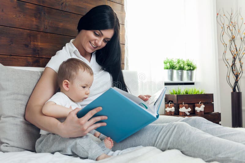 Kindererziehung Glückliche Mutter mit ihrem Kleinkind, das auf dem Bett sitzt und ein Buch liest lizenzfreie stockbilder Kindererziehung Glückliche Mutter mit ihrem Kleinkind, das auf dem Bett sitzt und ein Buch liest lizenzfreie stockbilder