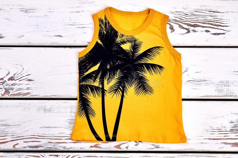 Kids yellow printed t-shirt. Childrens sleeveless t-shirt with a pattern of palm trree on white wooden ackground. Childs summer outfit. Kids yellow printed t-shirt. Childrens sleeveless t-shirt with a pattern of palm trree on white wooden ackground. Childs summer outfit.